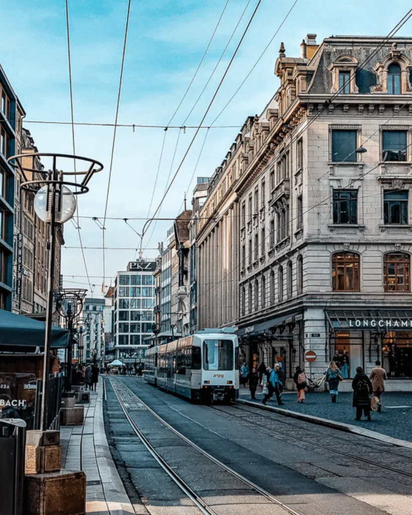 A tram travels down a historic Swiss city street lined with classic stone buildings.