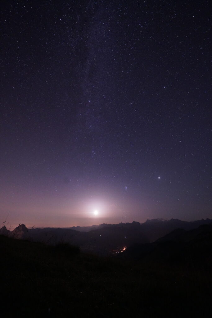 A starry night sky over the Swiss Alps with bright city lights reflecting in the lake below Fronalpstock.