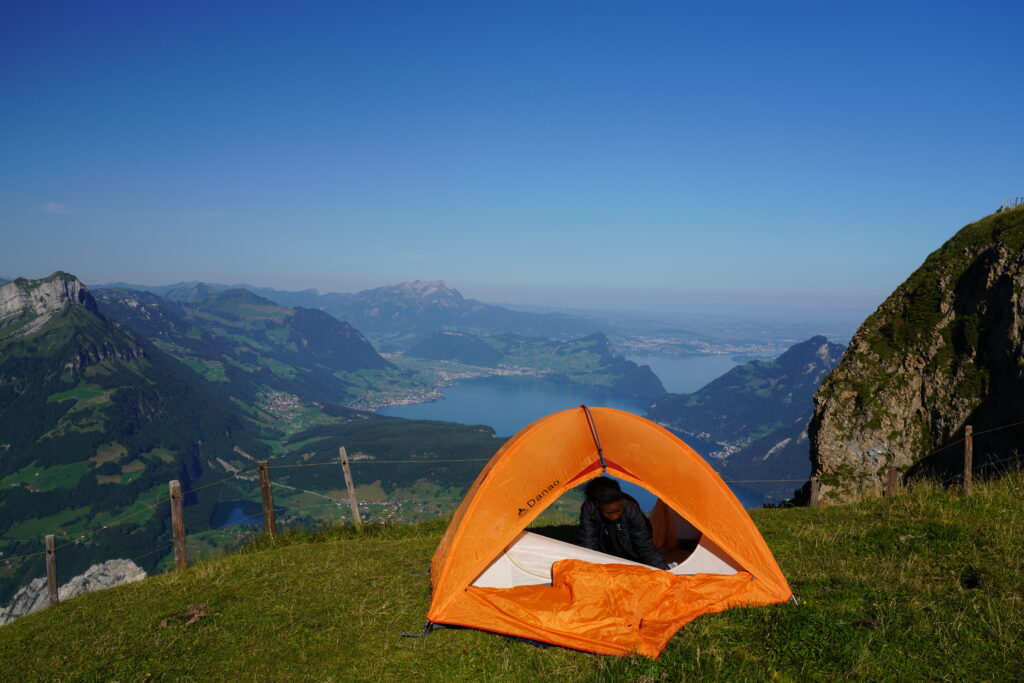 An orange tent set up on a grassy ridge overlooking the beautiful blue waters of Lake Lucerne in Switzerland.