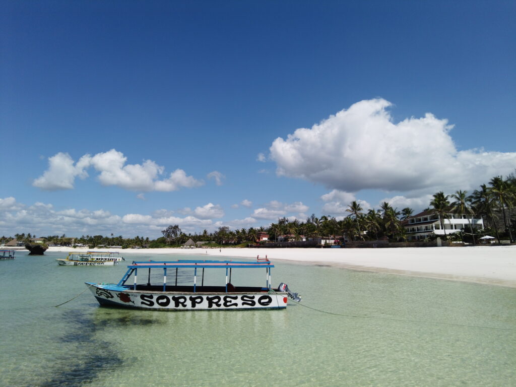 A glass-bottom tour boat resting on the pristine white sand of a Watamu beach under a bright blue sky.