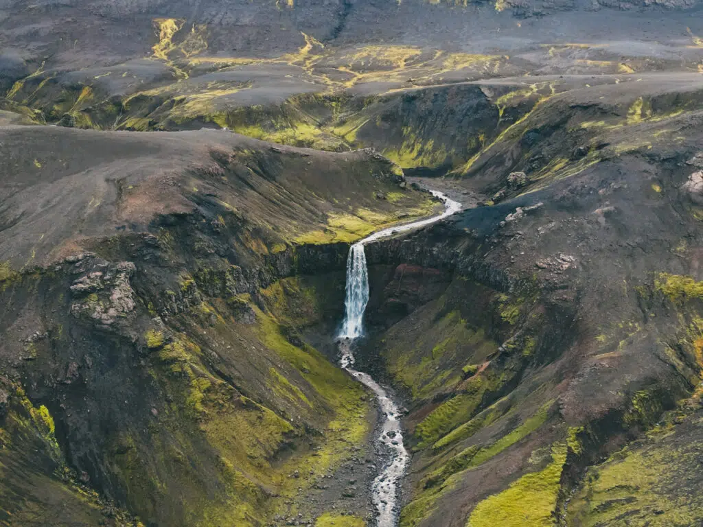A wide shot of a waterfall flowing down a rocky canyon into a valley.